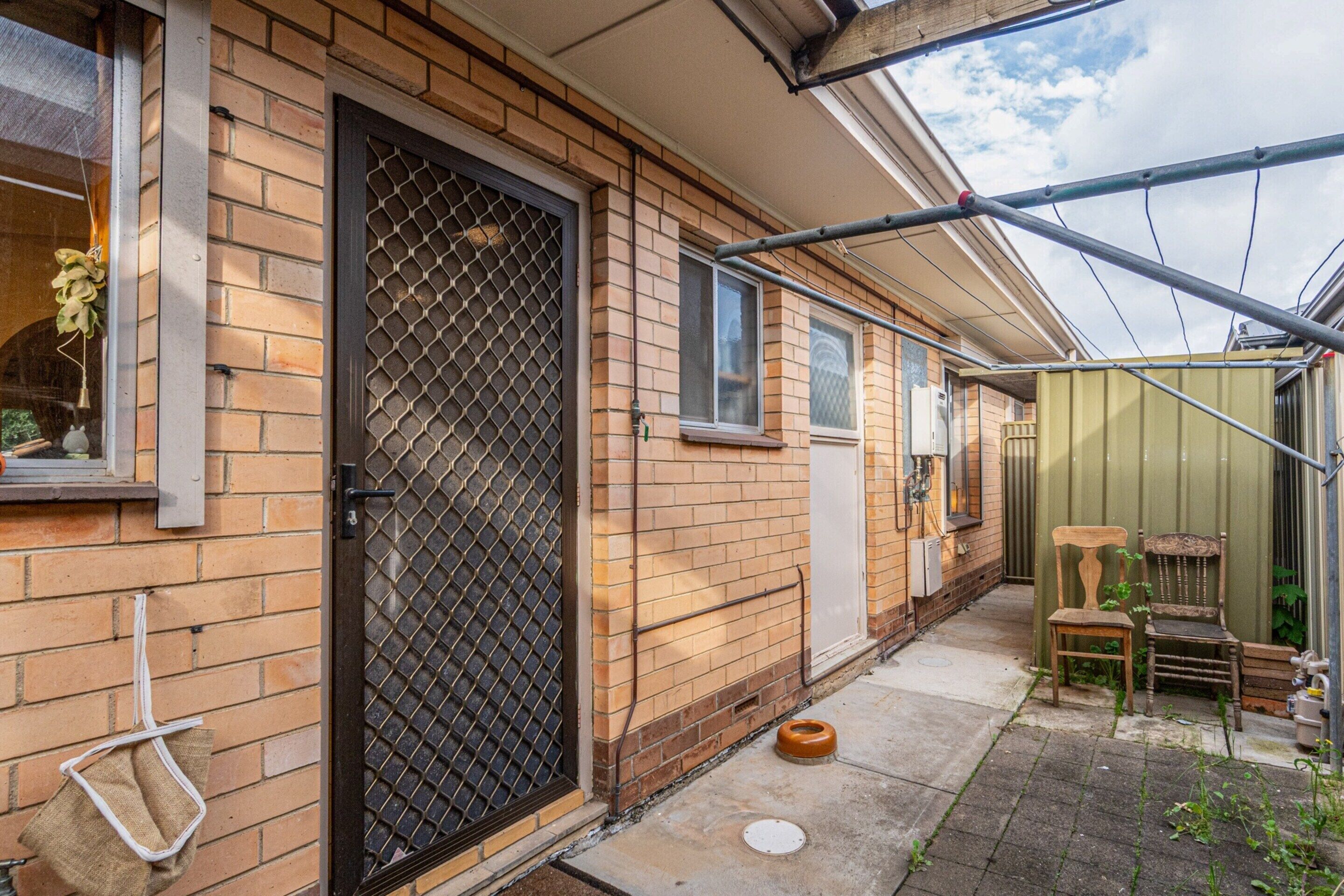 A brick house with a black door, a small window, and a metal gate.