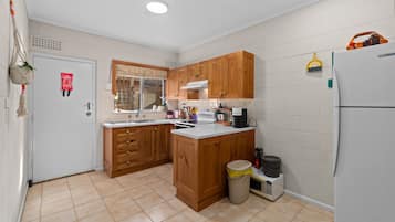 A compact kitchen with wooden cabinets, a white refrigerator, and a trash bin.