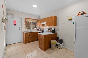Eine kleine Küche mit Holzschränken, einem weißen Kühlschrank und einem Mülleimer.