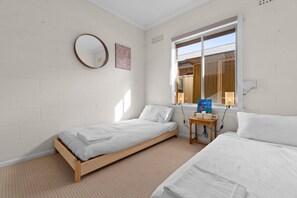 A bedroom with two single beds, a round mirror, a window with a view, and a small table with a book. - Courtyard 2 Bed Apartment Mile End (Adelaide)