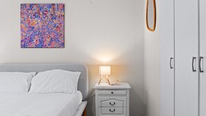 Ein Schlafzimmer mit einem Bett, einem Nachttisch mit Lampe, einem Kleiderschrank und einem farbenfrohen abstrakten Gemälde an der Wand.