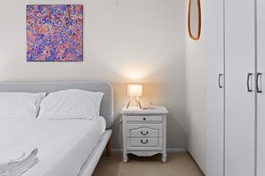 Ein Schlafzimmer mit einem Bett, einem Nachttisch mit Lampe, einem Kleiderschrank und einem farbenfrohen abstrakten Gemälde an der Wand.