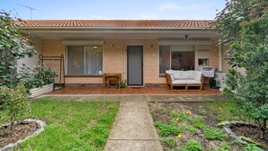 Ein Wohnhaus mit Ziegeldach, Ziegelaußenwand, überdachter Terrasse mit Sofa und Tisch sowie einem Garten mit Weg.