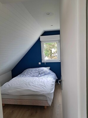 A bedroom with a sloped ceiling, a single bed, a window, and a visible electrical outlet. - A beautiful 2-room apartment facing the ocean (Piriac-sur-Mer)