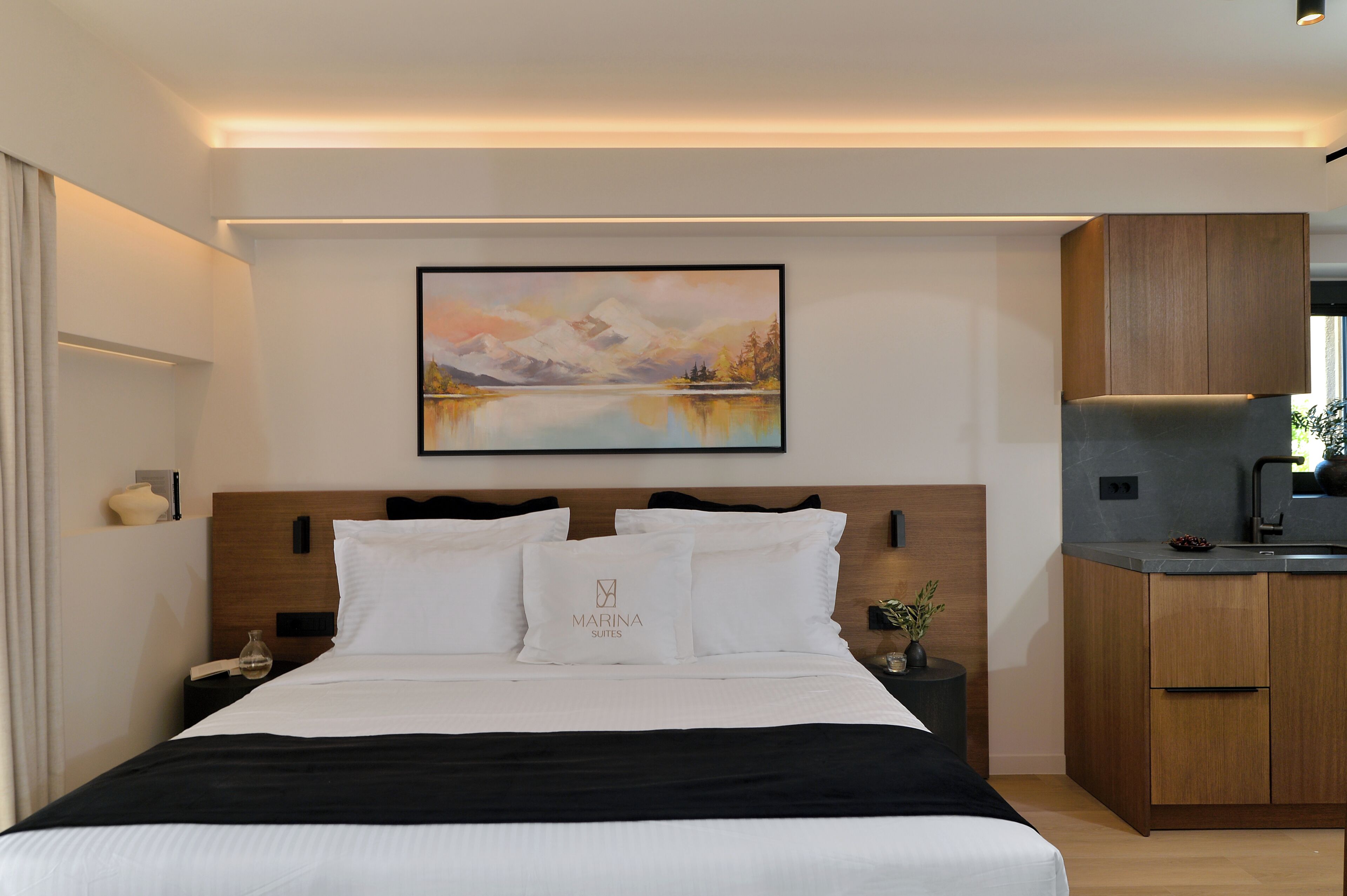 Habitación de hotel con cama, un cuadro, mesita de noche, un florero y vistas al exterior.