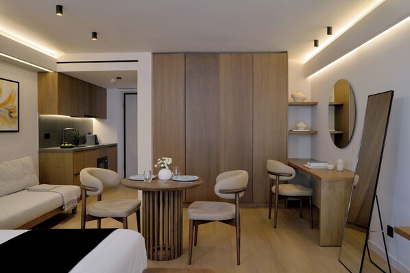 A modern hotel room with a bed, a dining table with chairs, a small kitchen area, and a large mirror. - Marina Suites Athenian Riviera (Alimos)