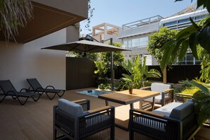 A modern outdoor seating area with lounge chairs, a table, and a hot tub. - Marina Suites Athenian Riviera (Alimos)