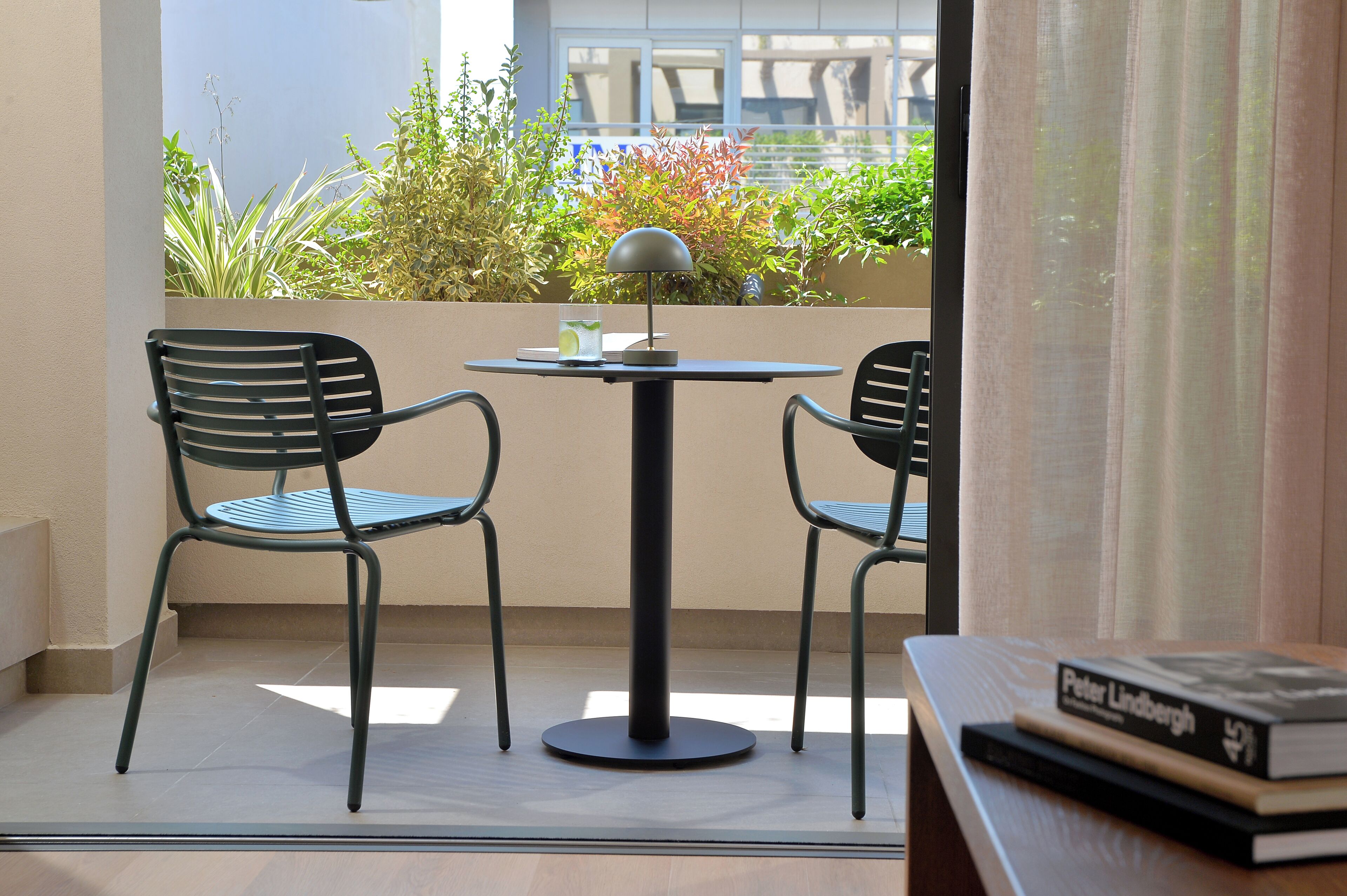 Uma varanda com duas cadeiras, uma mesa e um abajur. Há um livro sobre a mesa.