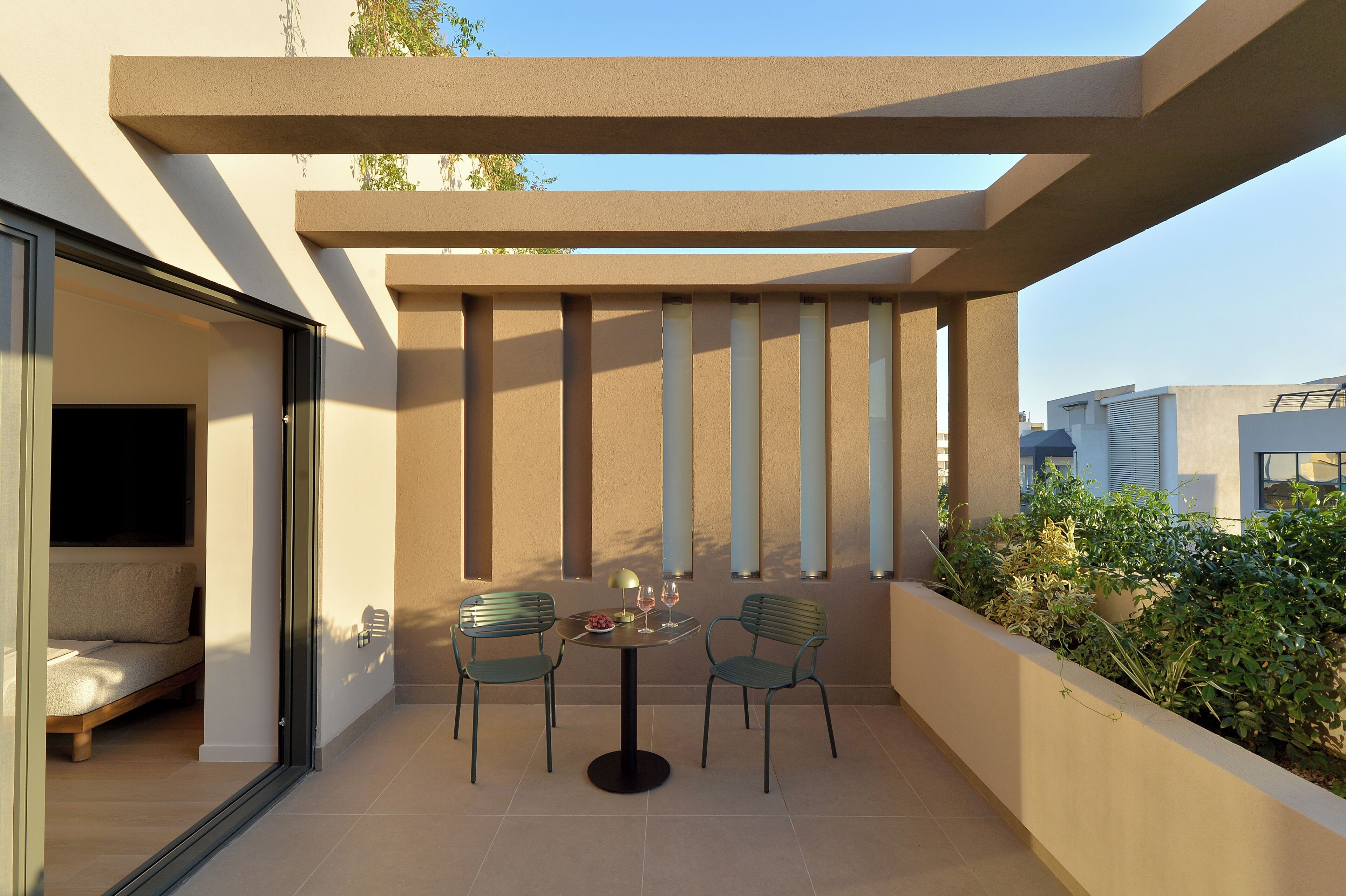 Un patio exterior moderno con una mesa y sillas, un ventanal de vidrio que da a una habitación y vistas panorámicas de la ciudad.
