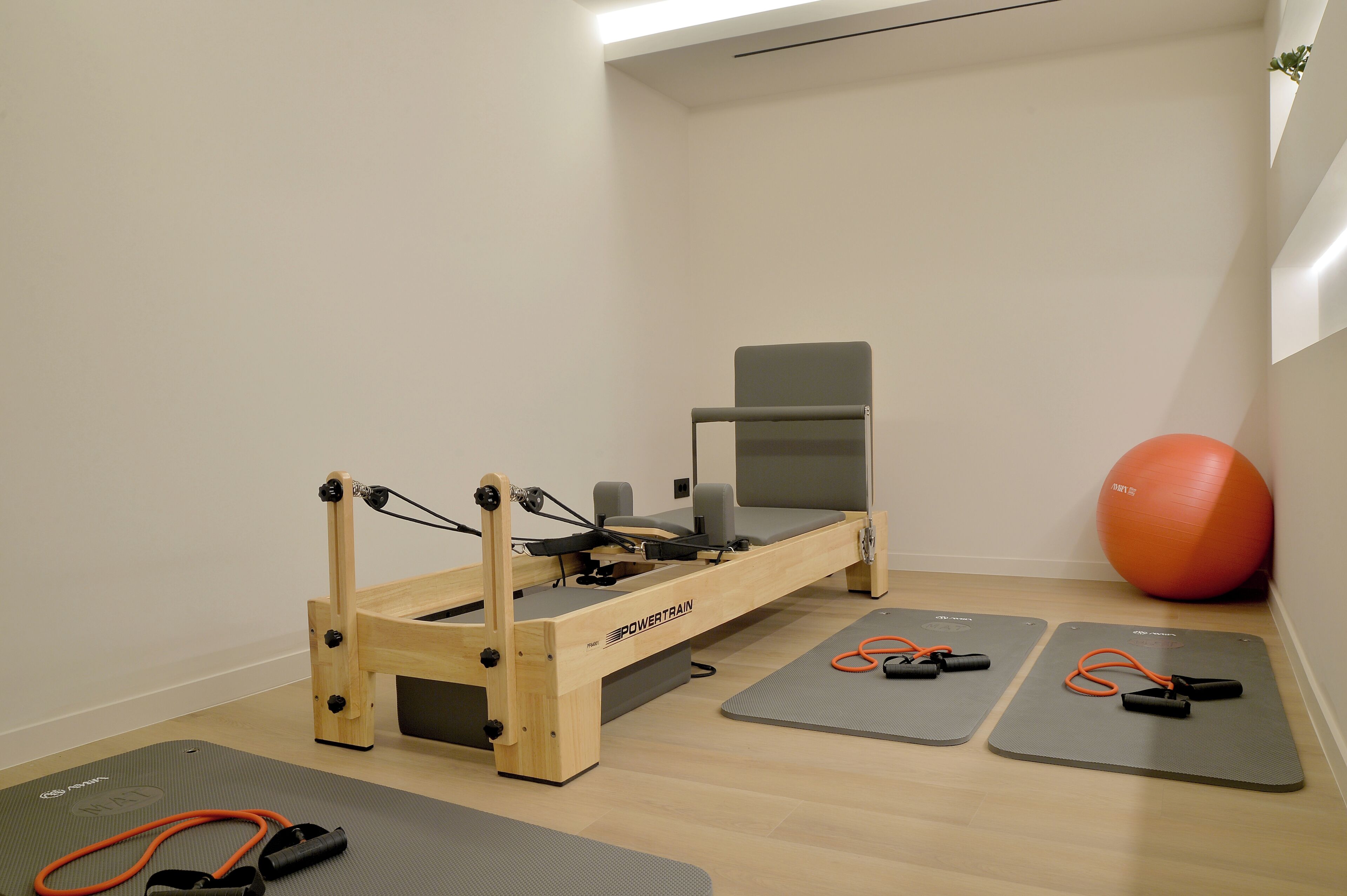 Une pièce comprenant une table de massage en bois, deux tapis de sol pour les exercices, une chaise grise et un ballon d’exercice orange.