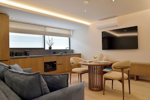 A modern kitchen with a dining area, a flat-screen TV mounted on the wall, and a sofa in the foreground.