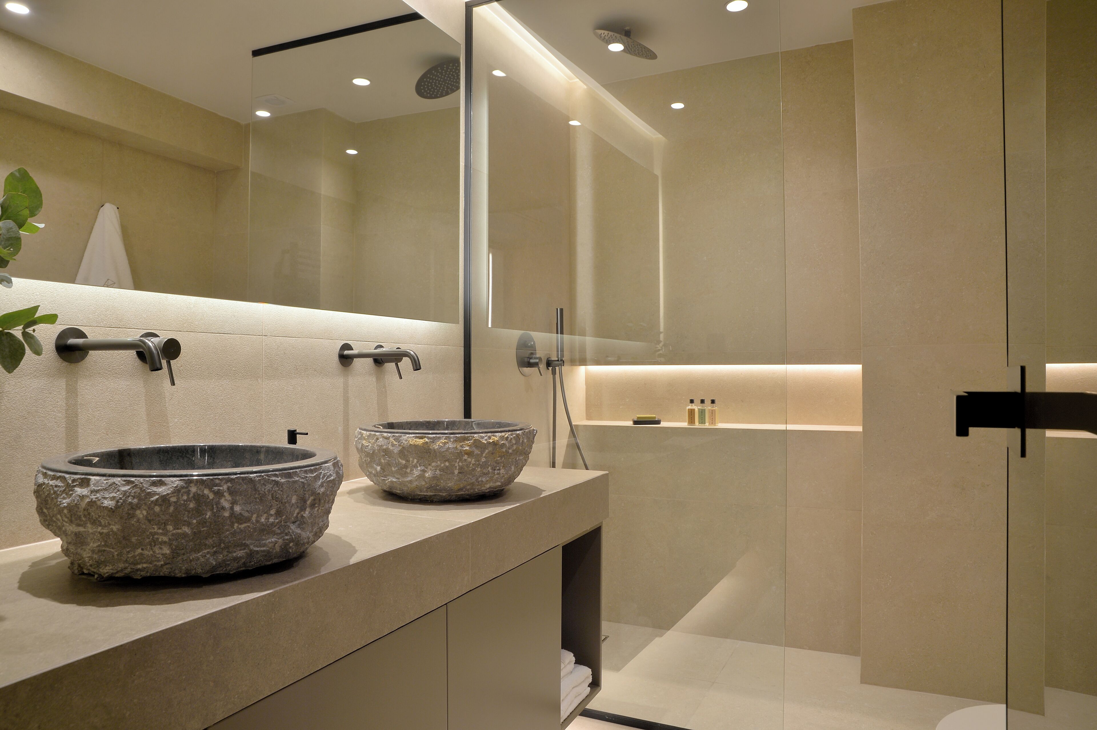 A modern bathroom with two stone sinks, a glass shower enclosure, and a minimalist design.
