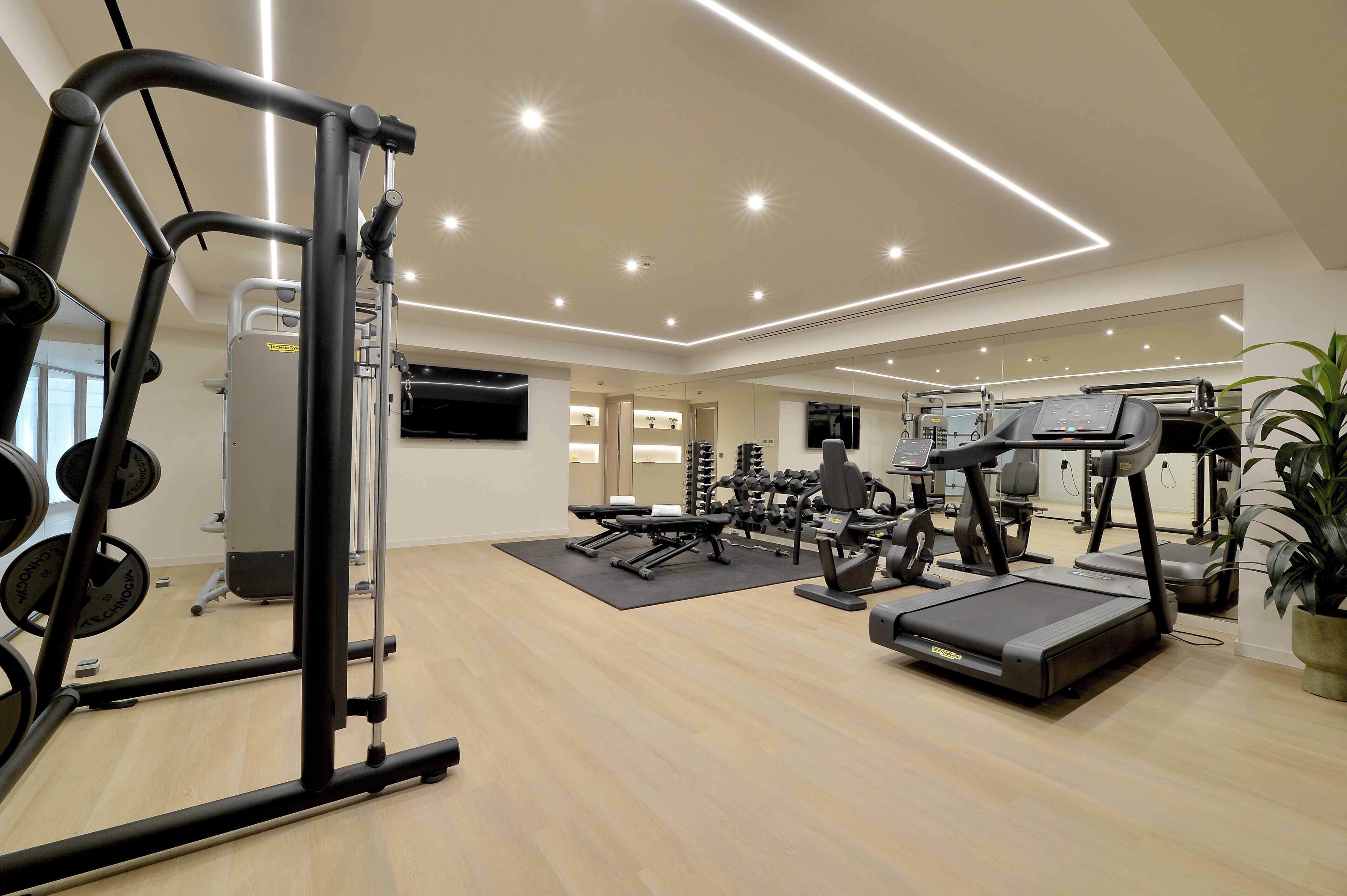 A modern gym with various exercise equipment, a flat-screen TV, and a large mirror.