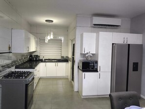 A modern kitchen with white cabinets, a gas stove, a microwave, and a refrigerator. - Chic Blue Oasis Modern Curaçao Willemstad Retreat (Willemstad)