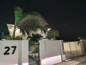 A gated entrance with a number '27' sign, a modern building with a white facade, and palm trees. - Chic Blue Oasis Modern Curaçao Willemstad Retreat (Willemstad)
