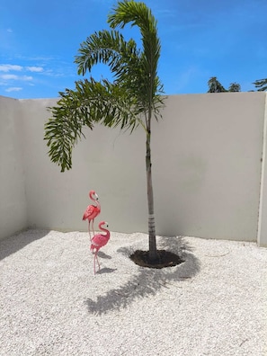 A small palm tree in a planter with two pink flamingos standing beside it. - Chic Blue Oasis Modern Curaçao Willemstad Retreat (Willemstad)