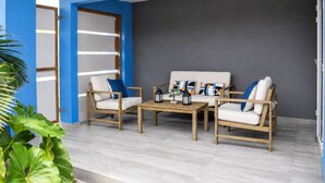 Un espacio exterior moderno con una zona de estar, un sofá, dos sillones, una mesita y cojines decorativos.