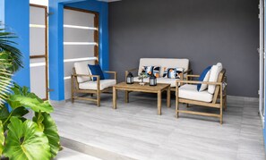 Ein moderner Außenbereich mit Sitzgelegenheiten, einer Couch und zwei Sesseln, einem kleinen Tisch und dekorativen Kissen.