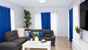 Una sala moderna con un sofá seccional gris, una mesa de centro blanca y cortinas azules.