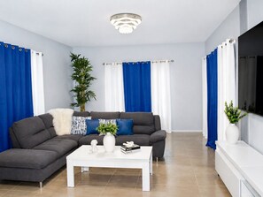 Ein modernes Wohnzimmer mit einem grauen Ecksofa, einem weißen Couchtisch und blauen Vorhängen.
