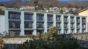A modern multi-story building with balconies, a stone retaining wall, and a mountainous backdrop.