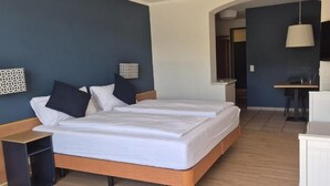 A hotel room with a double bed, a desk, a chair, a TV, and a small kitchenette.