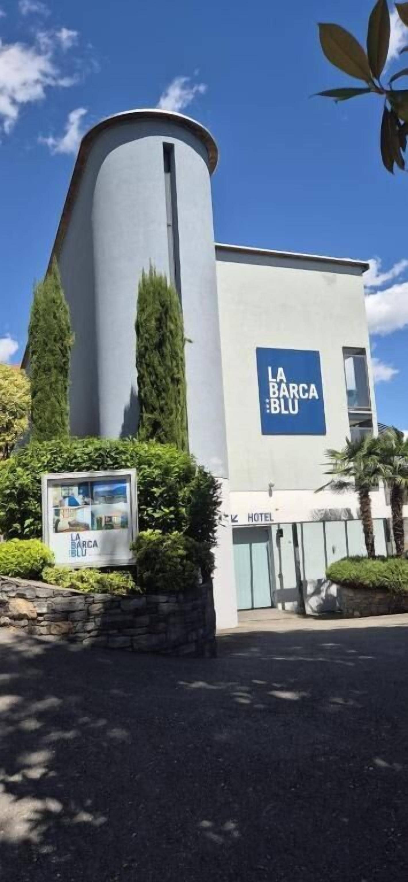 Un edificio moderno con fachada curva, un letrero que dice 'LA BARCA BLU' y la entrada del hotel.