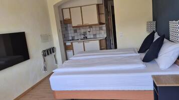 Un dormitorio con cama, televisor montado en la pared, una kitchenette pequeña y un baño visible a través de una puerta abierta.