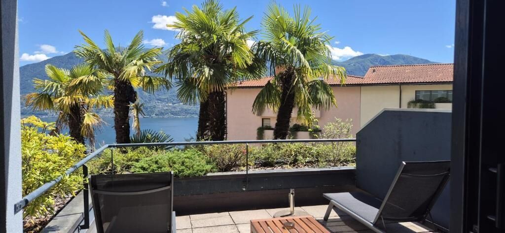 Un balcón con vista a un lago y montañas, amueblado con una mesa y sillas.