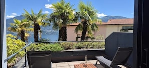 Un balcón con vista a un lago y montañas, amueblado con una mesa y sillas.