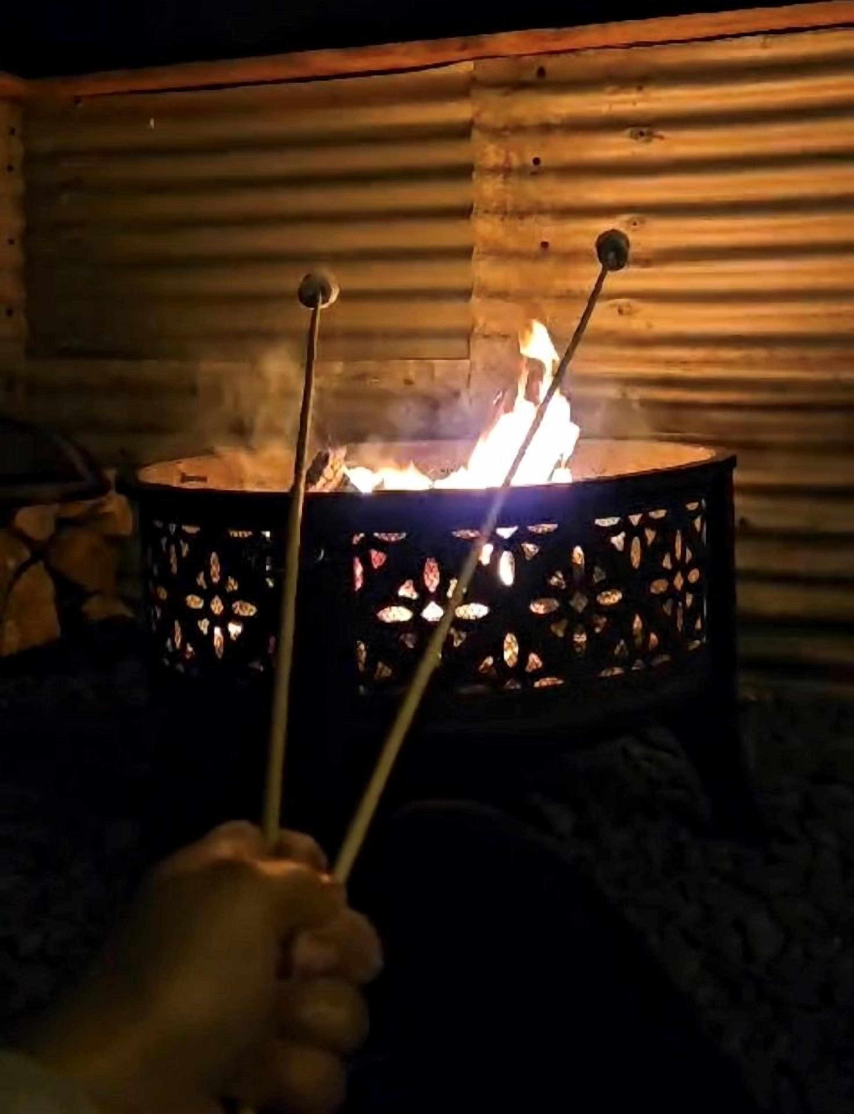 Une main tenant deux bâtons au-dessus d’un feu dans un récipient en métal, avec un fond en bois.
