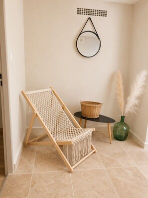 A room with a wooden hammock chair, a small round mirror, a wicker basket, and a green vase with pampas grass.