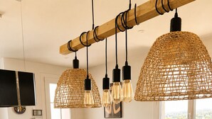 A modern kitchen with a dining table, hanging rattan light fixtures, and a fruit display.