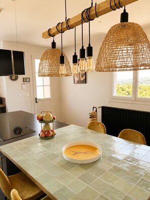 A modern kitchen with a dining table, hanging rattan light fixtures, and a fruit display.