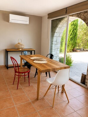A dining area with a wooden table, red and white chairs, a small table with a lantern, and a view of greenery through a glass door.