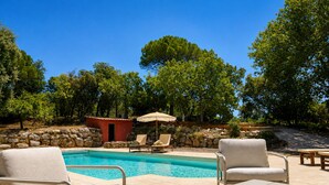 A swimming pool with lounge chairs and a small red building, surrounded by trees.