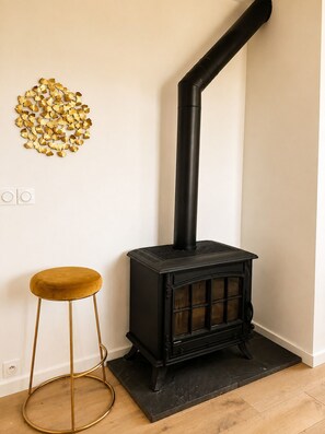 A black wood-burning stove with a chimney, a gold-colored stool, and a decorative gold leaf wall art piece.