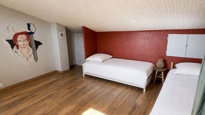 A room with two beds, a red accent wall, and a wooden floor.
