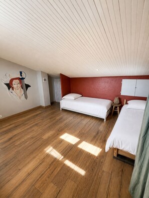A room with two beds, a red accent wall, and a wooden floor.