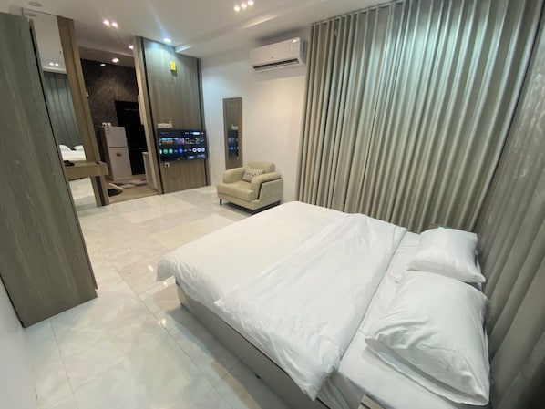 Una habitación de hotel moderna con una cama grande, una zona de estar con sofá, un televisor y un baño con espejo e inodoro.