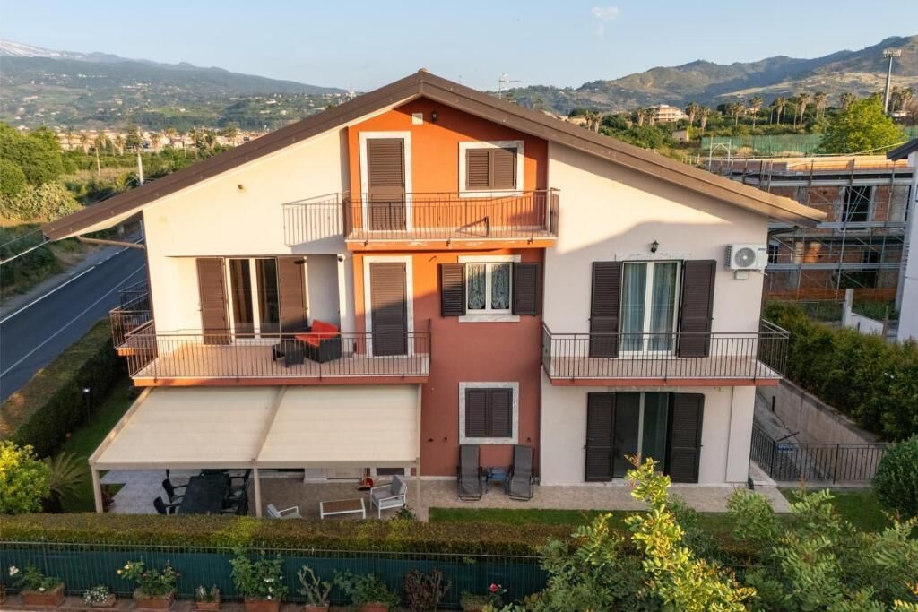 A two-story residential building with a balcony on the upper floor, a covered patio area, and a view of the surrounding landscape.