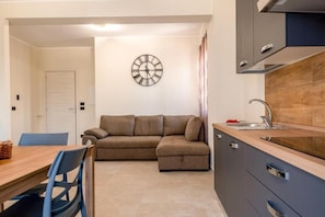 A compact living space with a kitchenette, a sofa, a dining table, and a wall clock. - Family House Turiddu (Fiumefreddo Sicilia)
