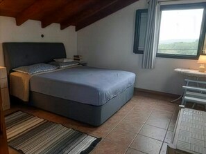 A bedroom with a bed, a bedside table, a lamp, and a view through a window.