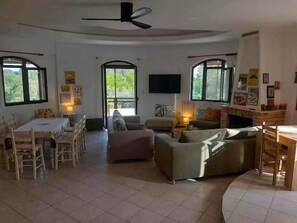 A spacious living area with a dining table, sofas, a TV, and large windows.