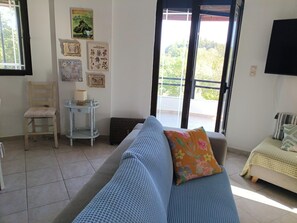 A living room with a sofa, a chair, a small table, and a window with a view of greenery.