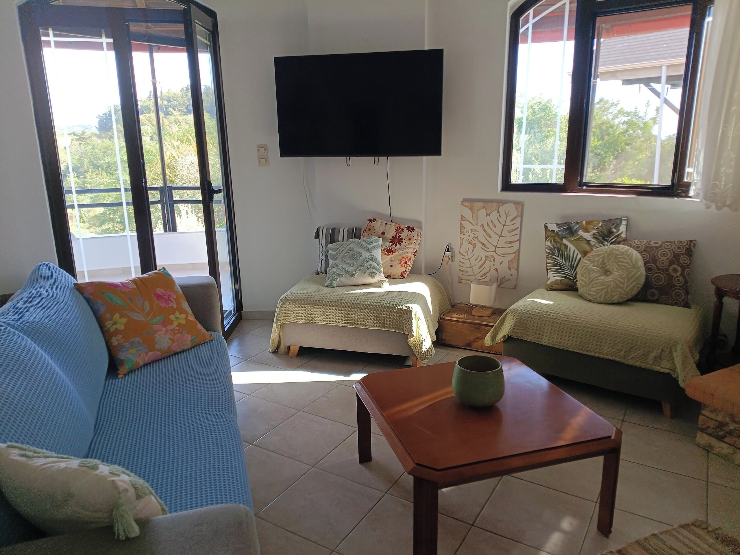 A living room with a sofa, a small table, a bed, and a TV mounted on the wall.