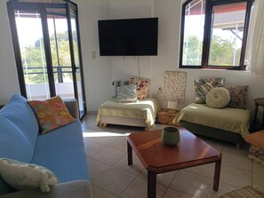 A living room with a sofa, a small table, a bed, and a TV mounted on the wall.