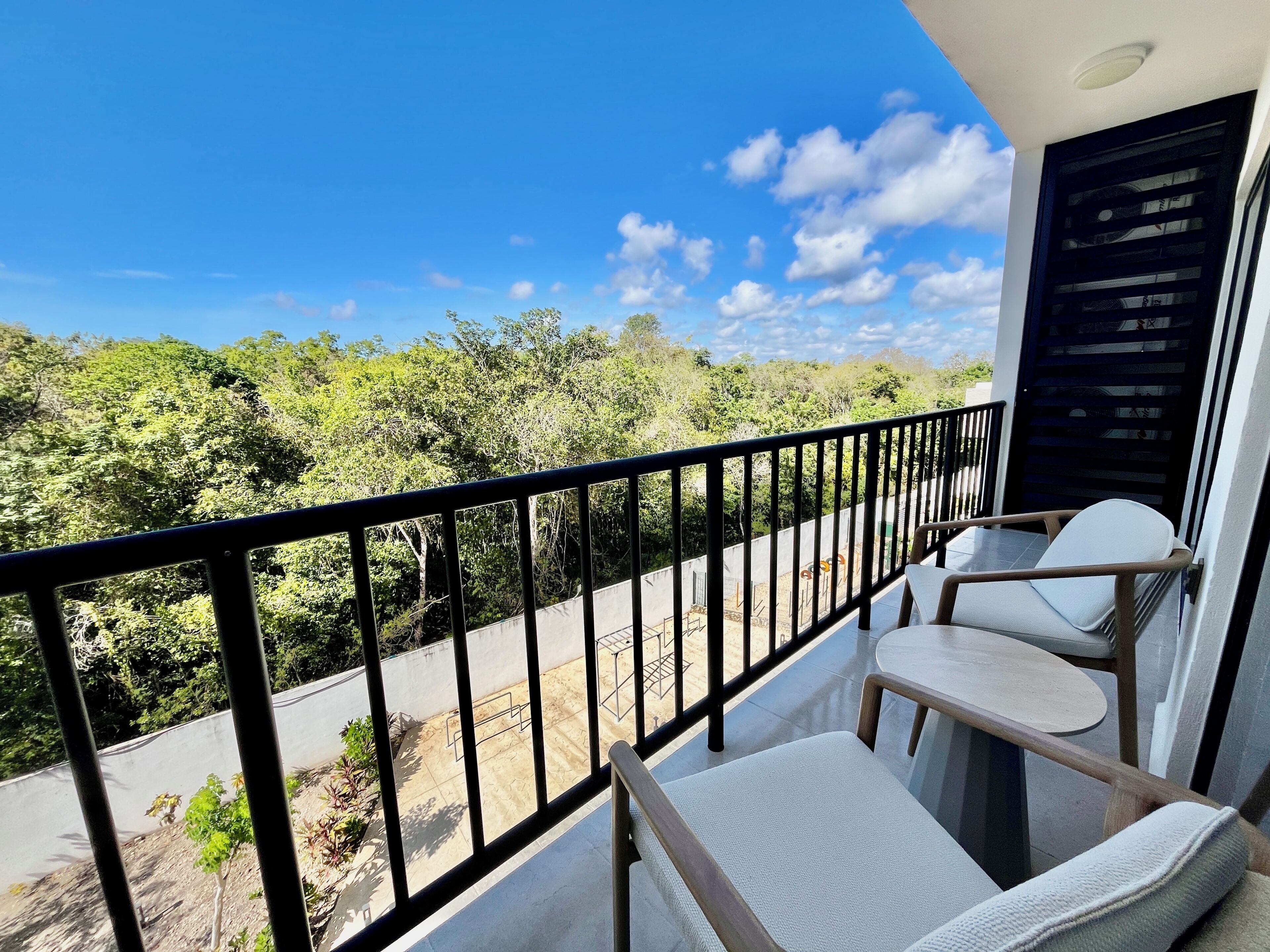A balcony with a view of a green landscape, a black railing, and two white chairs.