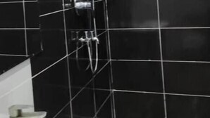 Un baño con un lavamanos blanco, paredes de azulejos negros y una zona de ducha.