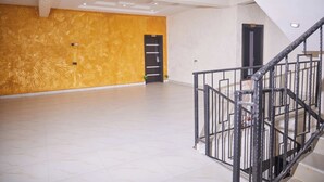 Una habitación amplia con diseño moderno, que presenta una pared con textura de madera, una escalera con barandillas metálicas y un suelo de baldosas.